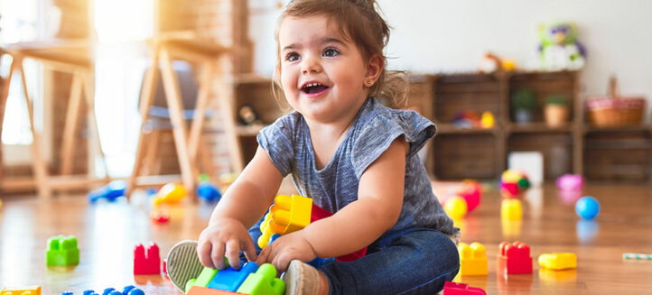 Beautiful toddler sitting on the floor playing with building blocks toys at kindergarten
