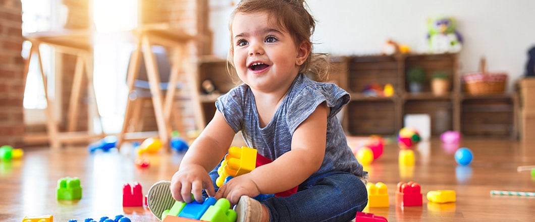 Beautiful toddler sitting on the floor playing with building blocks toys at kindergarten