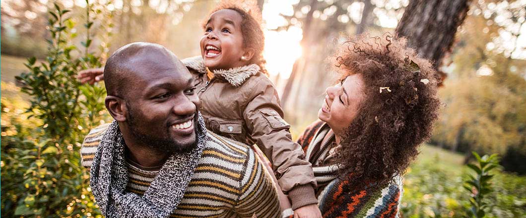 Happy African American family having fun in autumn day at the park. Father is piggybacking little girl.