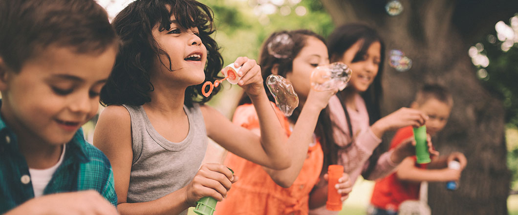 Long haired hispanic boy laughing and having fun with his friends standing on a wooden fence in a summer park blowing bubbles, with a vintage develop