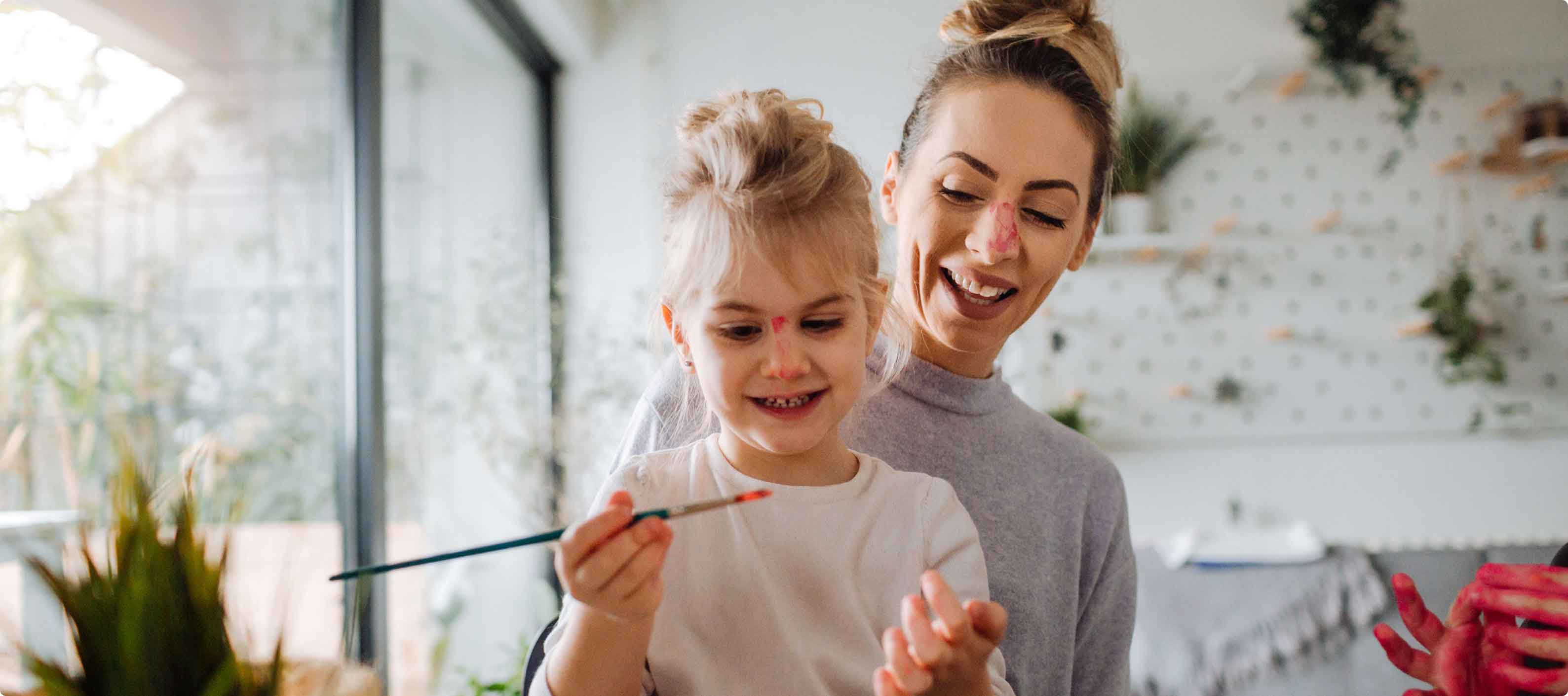 Mother and daughter having fun with a paintbrush and paint on both of their noses