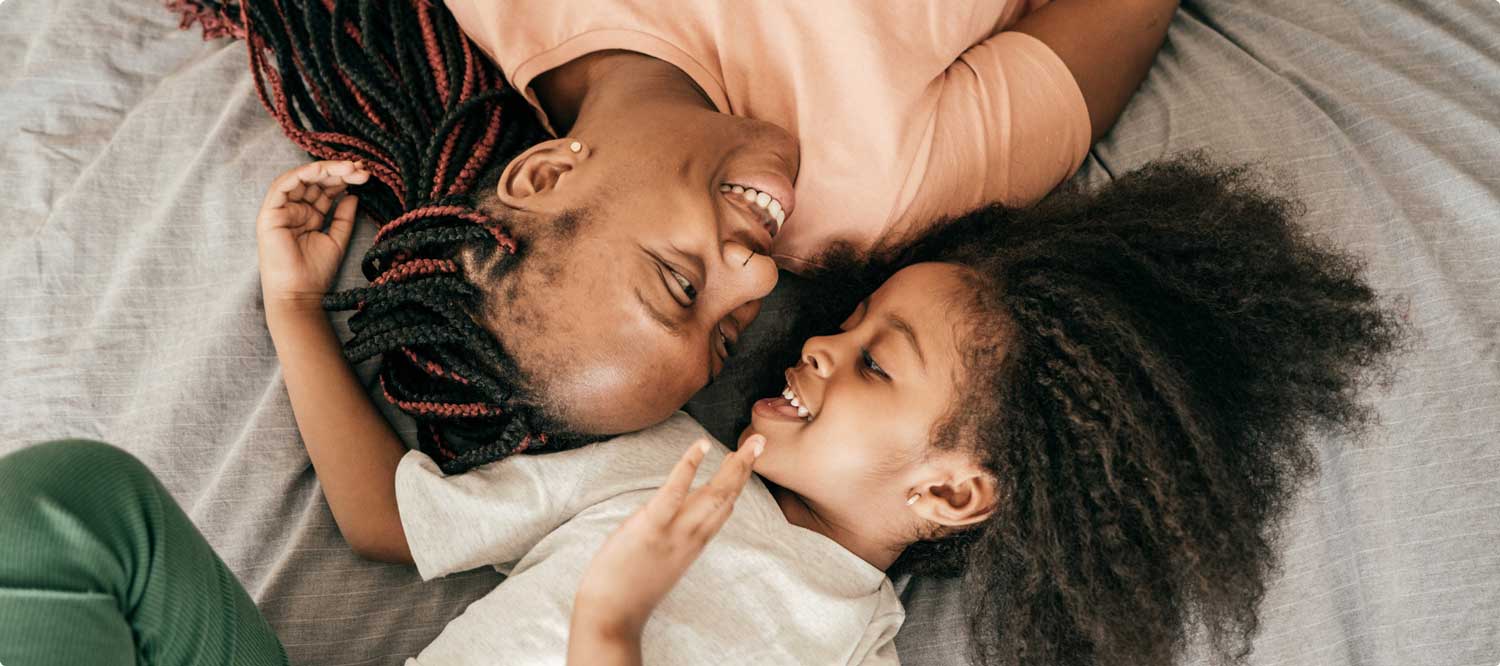 Affectionate African American mother and daughter laying on the floor smiling at each other