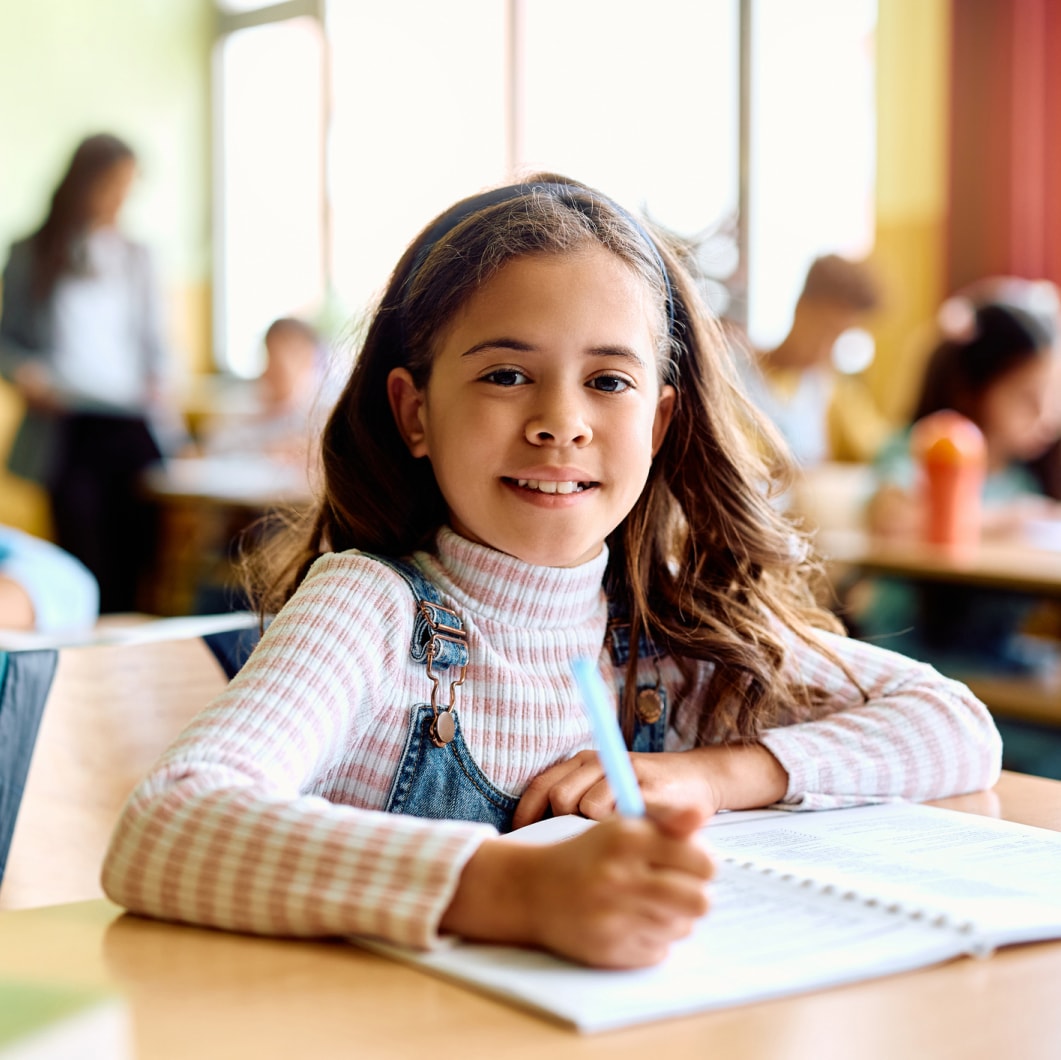 A young student smiling while working with a supportive therapist in a classroom environment.